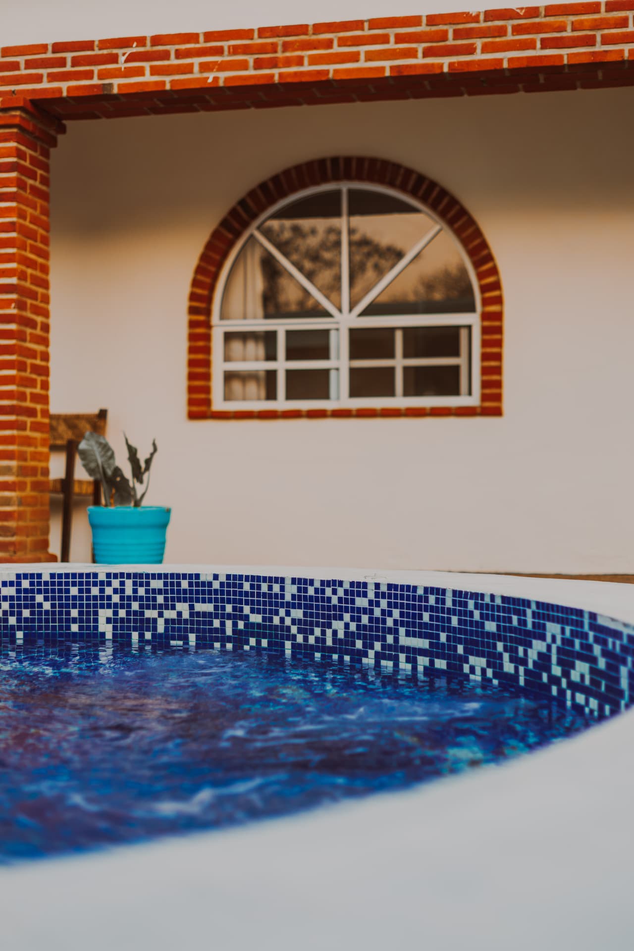 Jacuzzi de mosaico azul frente a la fachada de ladrillo con ventana de arco