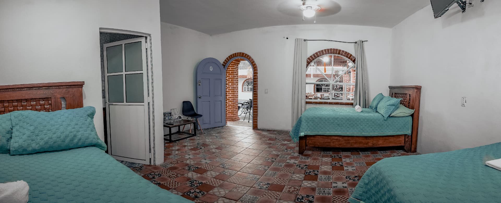 Habitación de Casa Arcos con dos camas, piso de mosaico y arco de ladrillo hacia la terraza